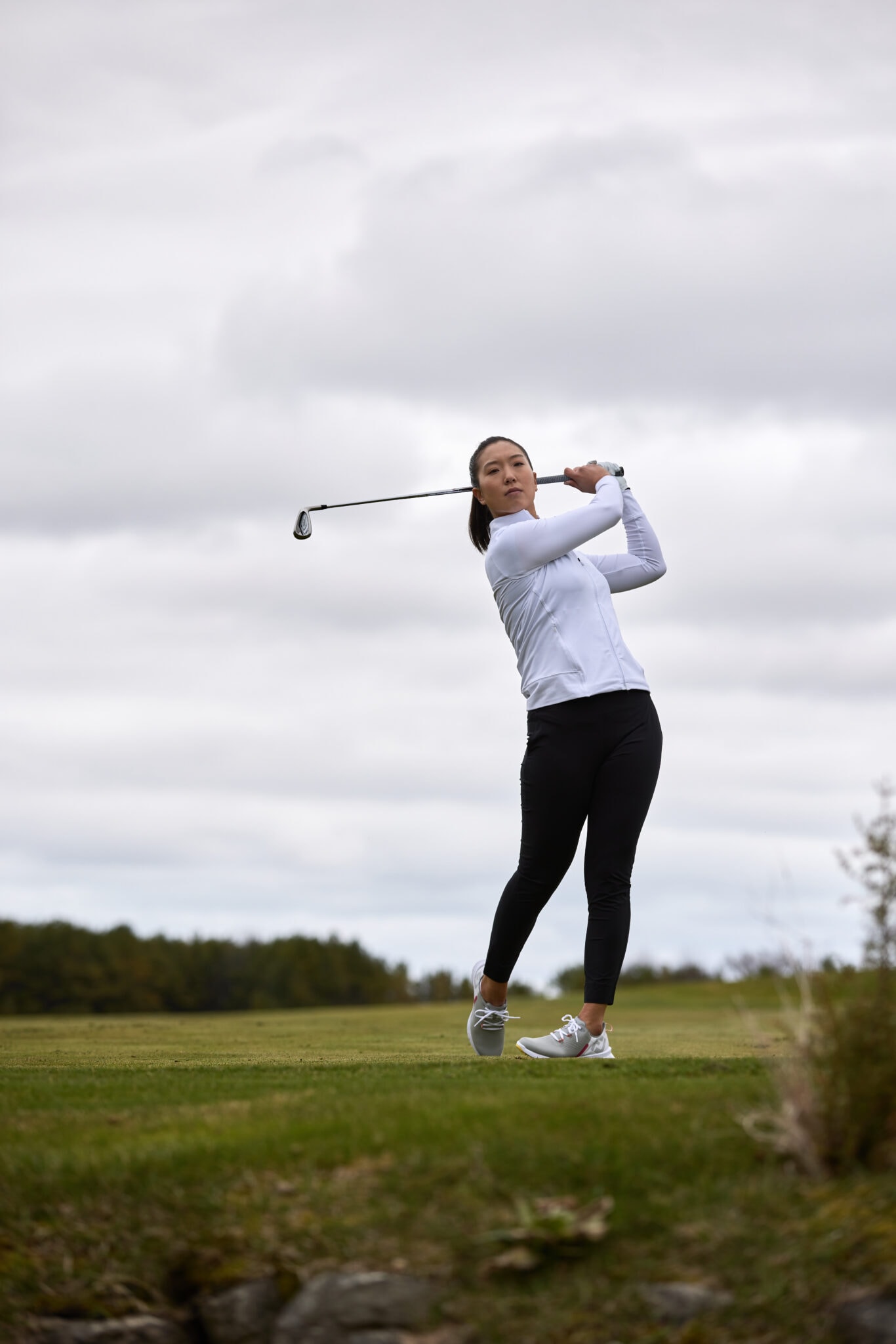 A woman swings a golf club wearing fashionable fitness gear for an advertising photo shoot.