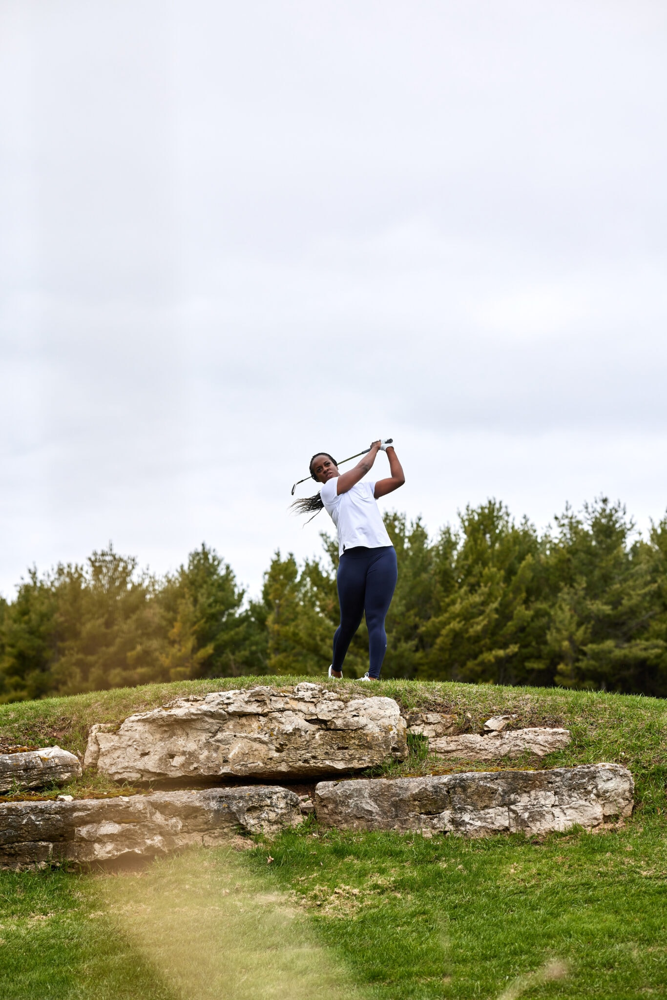 A woman swings a golf club over a rocky hill in an example of lifestyle fitness product photography.