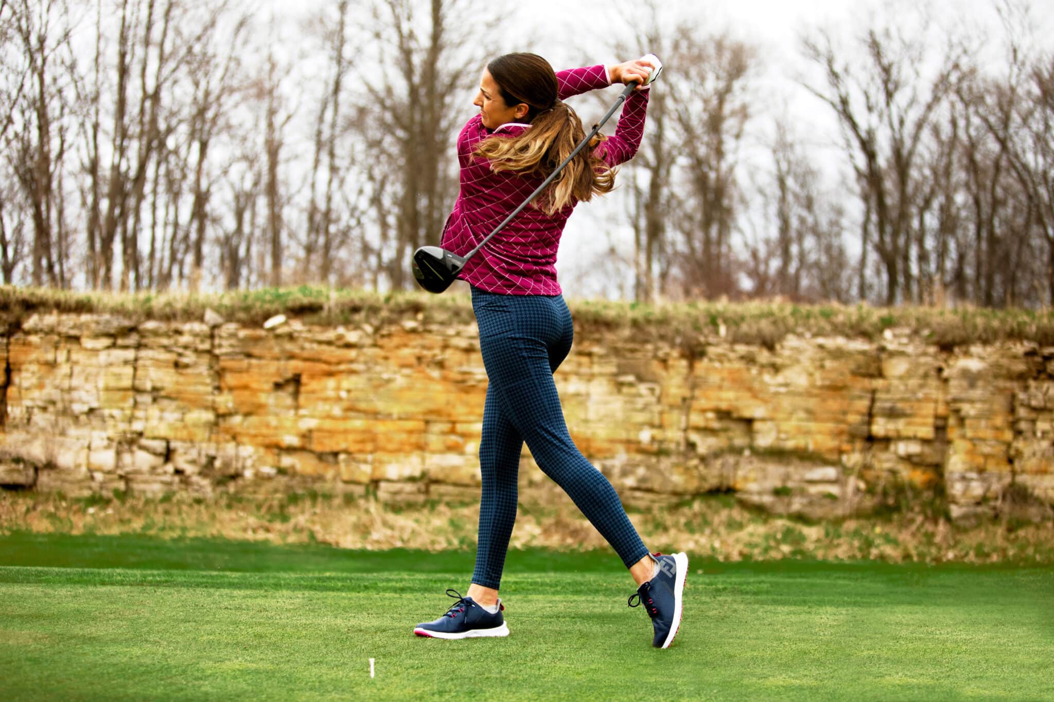 Brightly dressed woman swings a golf club. Image taken by fitness retail photographer Hannah Dunsirn.