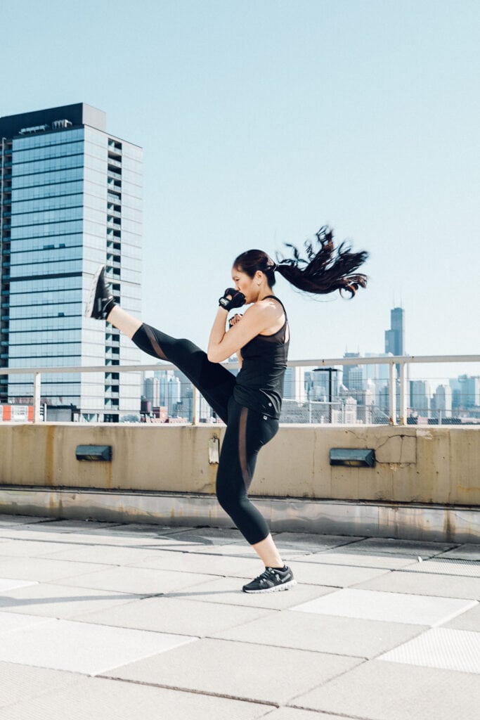 A woman practices kickboxing on the roof of a high rise building with a cityscape in the background. Photo taken by LA advertising photographer.