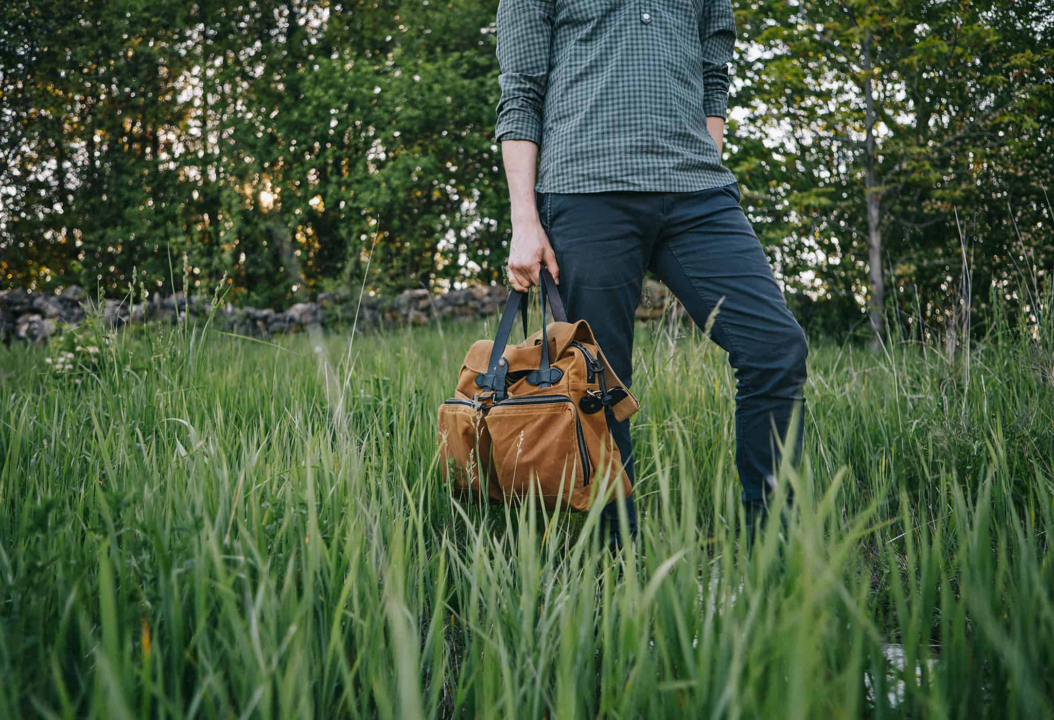 person holding brown duffel bag in tall field