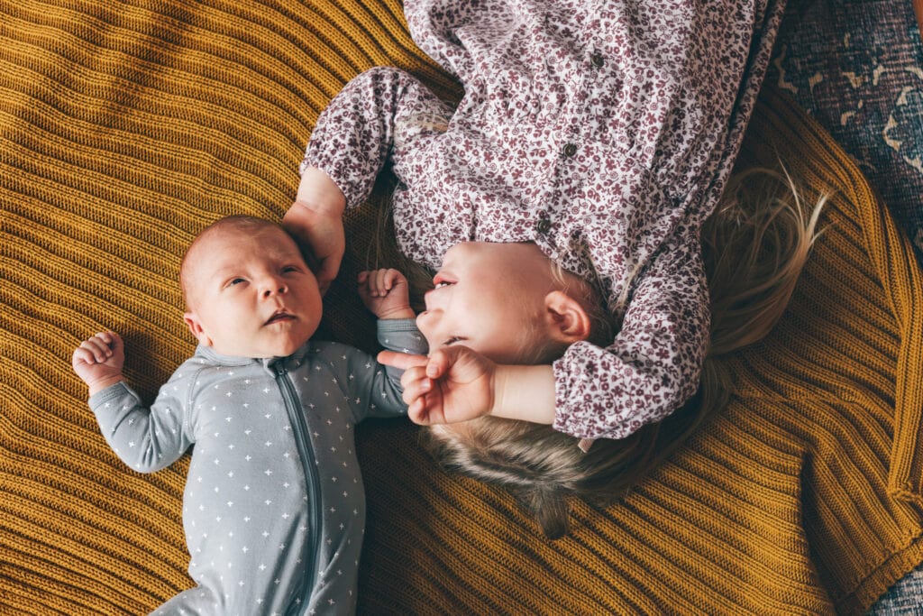 sister laying on bed pointing to infant brother