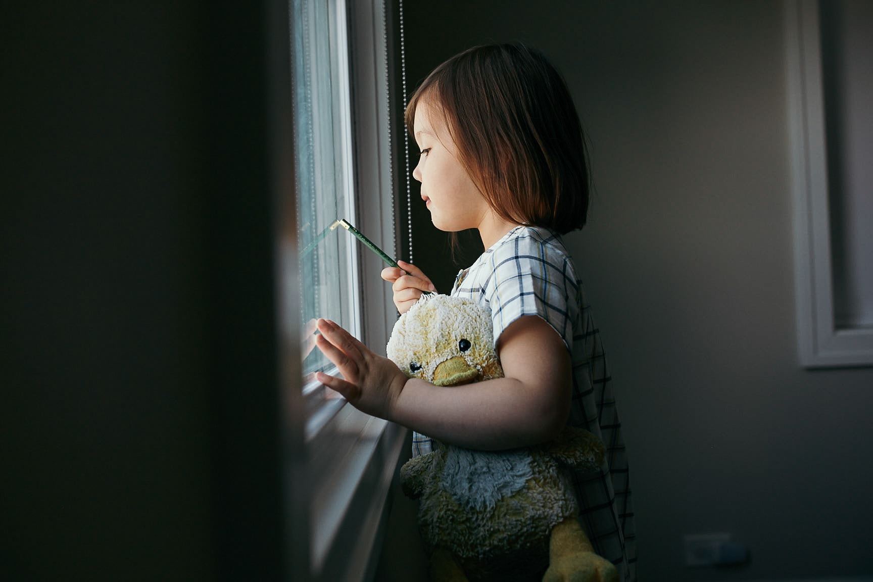 little girl looking out window holding a duck plushie