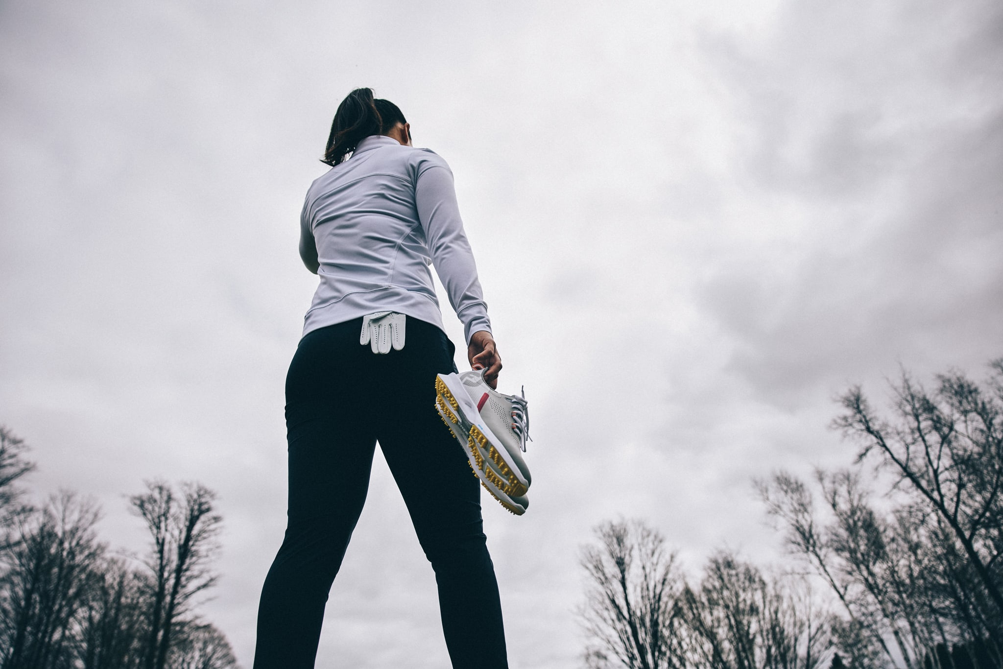 woman holding running shoes on a backdrop of a cloudy sky