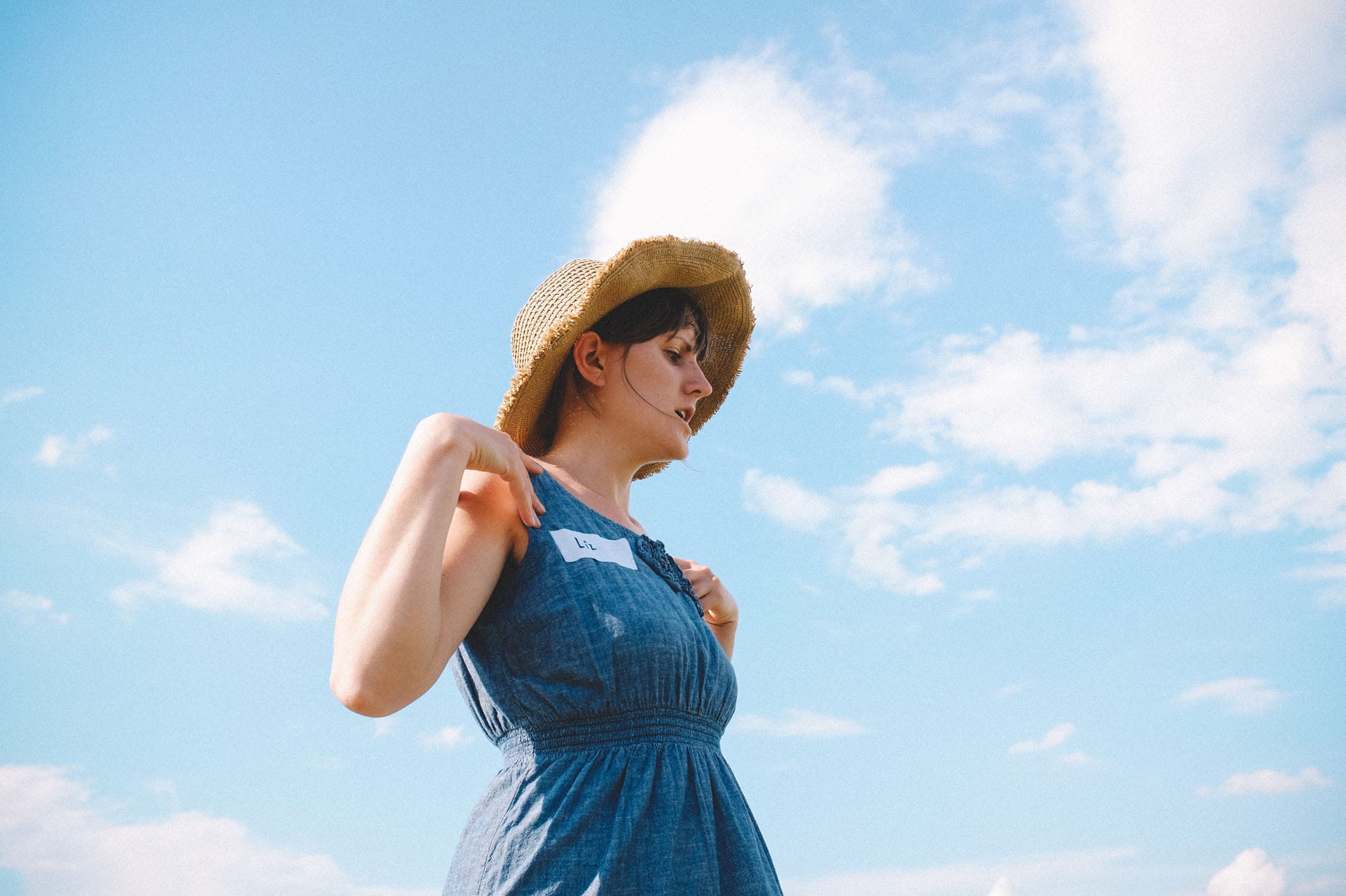 Image of a woman in a straw hat and blue dress behind a bright blue sky taken by an advertising lifestyle photographer